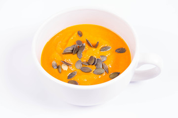 Pumpkin soup decorated with pumpkin seeds in a bowl on a white background
