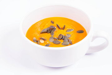Pumpkin soup decorated with pumpkin seeds in a bowl on a white background