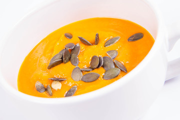 Pumpkin soup decorated with pumpkin seeds in a bowl on a white background