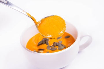 Pumpkin soup decorated with  pumpkin seeds being poured into a bowl on a white background