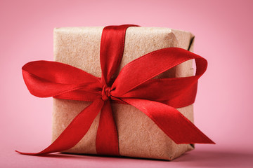 Gift tied with red ribbon on pink background close-up