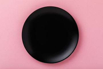 Black empty ceramic plate on pink table, top view. Food background