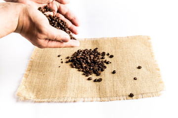 Man hands releasing a pile of coffee beans on a raffia cloth tablecloth on a white background
