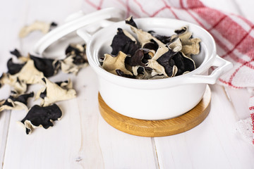 Lot of slices of dry black mushroom jew ear variety in a ceramic stewpan on white wood