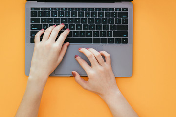 Women's hands type the text on the keyboard of the laptop on the orange background, the top view....