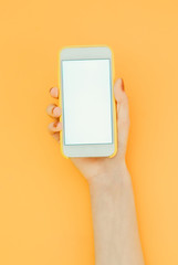 Fototapeta na wymiar Woman holds a smartphone with a white screen on the orange background, place for text on the smartphone screen. Copyspace. Flat lay