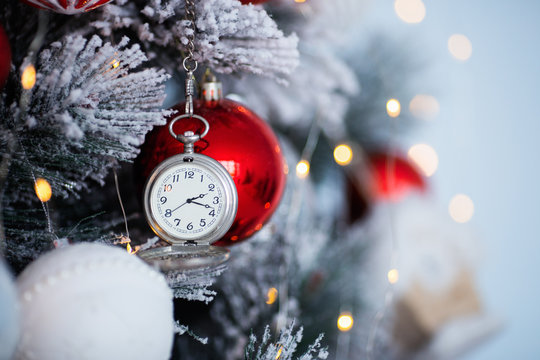 Vintage silver clock hanging on decorated Christmas tree with blurred bokeh background.