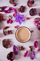 Violet cup of latte surrounded with purple dried flowers and petals, flat lay, top view