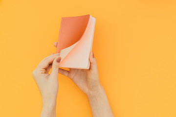 Woman opens a note of coral color on an orange background, hands with notebook a close-up....