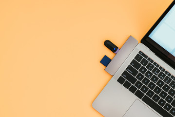 Modern laptop with USB Type-C adapter and flash drives is isolated on an orange background....