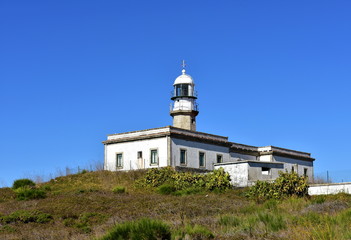 Old abandoned lighthouse with wind vane on a hill. Sunny day, blue sky. Galicia, Spain.