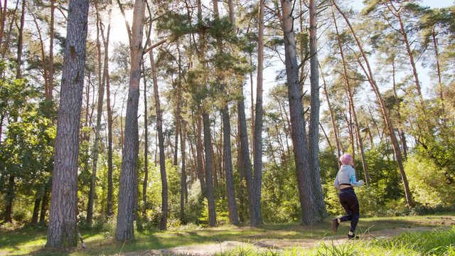 A young y with pink hair jogging in the forest. Long shot