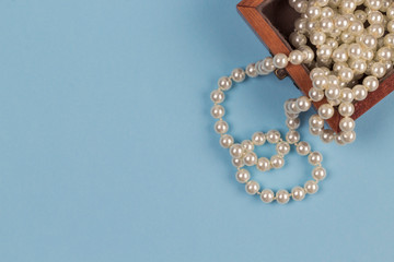 Pearl necklace in wooden box on light blue background. Copy space, top view, close-up