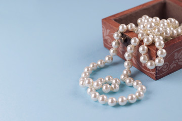Pearl necklace in wooden box on light blue background. Copy space, close-up, soft focus