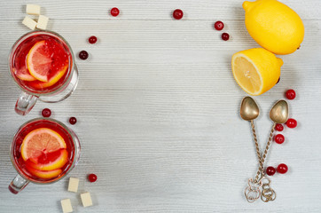 Fototapeta na wymiar Hot healthy winter drink - detox cranberry tea or sangria with fresh lemon slices in glasses on the gray concrete background. Top view with copy space for text