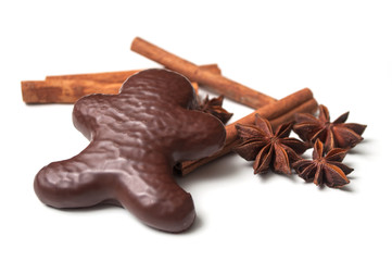 closeup of christmas gingerbread chocolate coated biscuit in shaped man with anise flower and cinnamon stick on white background
