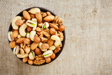 Mix of different nuts in a wooden cup against the background of fabric from burlap. Nuts as structure and background, macro. Top view.