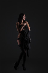 Fototapeta premium Sexy young brunette woman in black sensual lingerie posing on black background wall in studio.