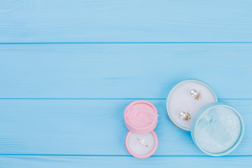 Ring with brilliant and earrings in round boxes. Copyspace. Blue wood background.