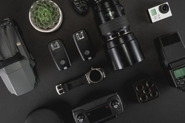 Work space photographer with laptop, digital camera, memory card, action camera, drone, remote controller, phone, VR glasses and camera accessory. Top view on black table background. 