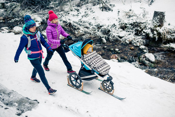 Two women with baby stroller enjoying winter in forest, family time