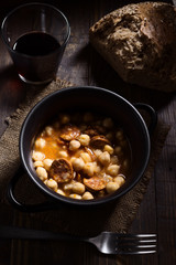 Vertical take of homemade chickpea stew with bread and wine on rustic wooden board illuminated in chiaroscuro