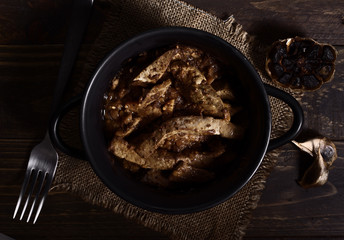 Homemade stew of lamb's liver and garlics on rustic wooden board illuminated in chiaroscuro