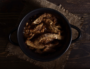 Homemade stew of lamb's liver on rustic wooden board illuminated in chiaroscuro