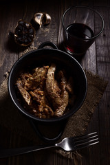 Homemade stew of lamb's liver with black garlics and red wine on rustic wooden board illuminated in chiaroscuro