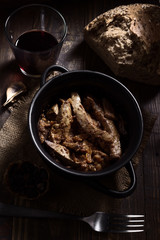 Homemade stew of lamb's liver with bread and red wine on rustic wooden board illuminated in chiaroscuro