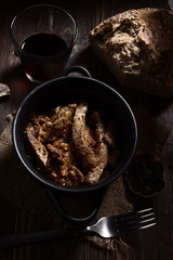 Homemade stew of lamb's liver with bread and red wine on rustic wooden board illuminated in chiaroscuro