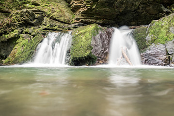 Obraz premium Small mountain waterfall on the rocks covered with moss in the forest