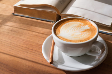 A Cup of hot latte art coffee on wooden table with book in coffee shop cafe.