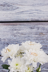 Fototapeta premium White chrysanthemum flowers on wooden background. Marriage proposal with bouquet of flowers and golden ring. Vintage effect.