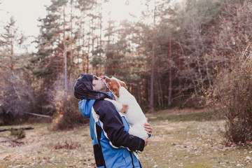 Fototapeta na wymiar Man with his cute small dog standing in the forest at sunset. healthy lifestyle. Hiking. Small dog kissing his owner
