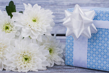 Close up white flowers and blue gift box. Bunch of white chrysanthemums and present box with white bow close up. Happy Valentines Day.