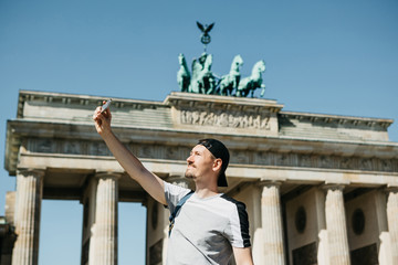 Tourist guy taking a selfie on the background of the Brandenburg Gate in Berlin in Germany or taking pictures of sights