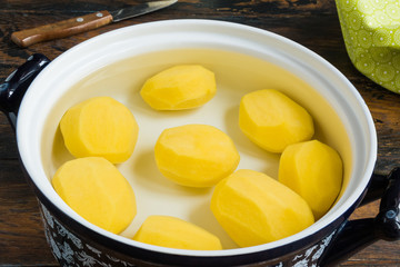 Peeled raw whole potatoes in pot with water