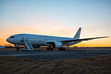 Fototapeta na wymiar White wide body passenger airplane with boarding steps at the airport apron in evening twilight