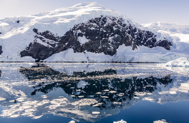Fototapeta na wymiar Snowy mountain peak and the glacier reflected in the Antarctic waters of Neco bay, Antarctica