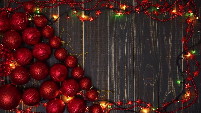 Top view flatlay of red shiny holiday decorations, lights of garland and empty copy space in wright side of frame. Real time 4k video footage.
