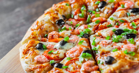 Pizza with Mozzarella cheese, olives, shrimps, tomato sauce, Spices and Fresh green onion. Italian pizza on wooden table background