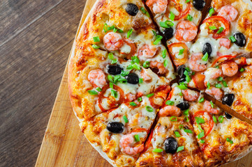Pizza with Mozzarella cheese, olives, shrimps, tomato sauce, Spices and Fresh green onion. Italian pizza on wooden table background