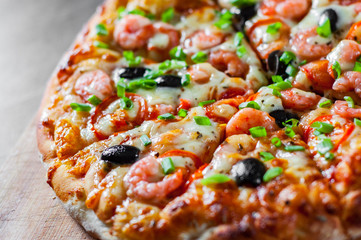 Pizza with Mozzarella cheese, olives, shrimps, tomato sauce, Spices and Fresh green onion. Italian pizza on wooden table background