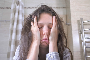 Woken tired woman in the bathroom with hangover and headache.