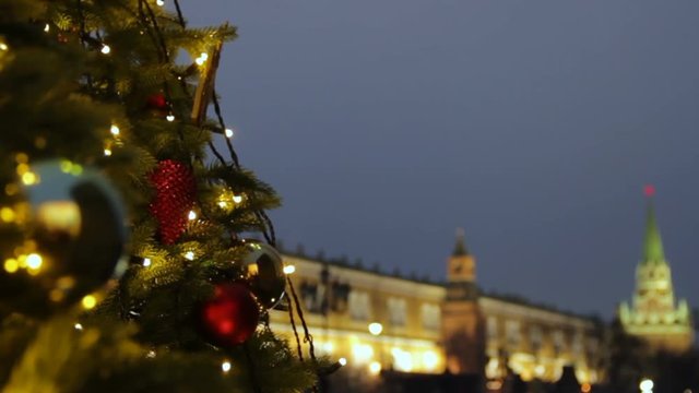 Holidays in Moscow. In the square a Christmas tree glows, decorated with balls and beautiful Christmas toys close-up. Kremlin tower, pedestrians and travellers walk on blurred background