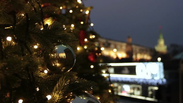 Holidays in Moscow. In the square a Christmas tree glows, decorated with balls and beautiful Christmas toys close-up. Kremlin tower, pedestrians and travellers walk on blurred background