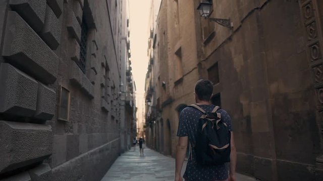 Male traveler is exploring old medieval buildings strolling on narrow street. He is examining architecture of Barcelona in Gothic Quarter