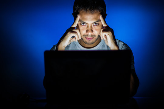 Man with laptop rubbing temples and looking at camera