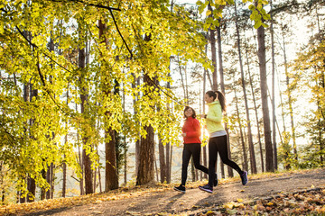 Two female runners jogging outdoors in forest in autumn nature.